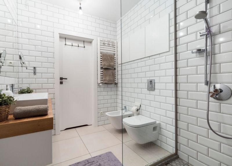 White ceramic bathroom tiling with matching white shower tiles and a wooden sink bench