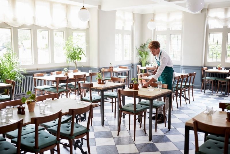 Waiter arranging a restaurant table on a black and white marble tiled floor