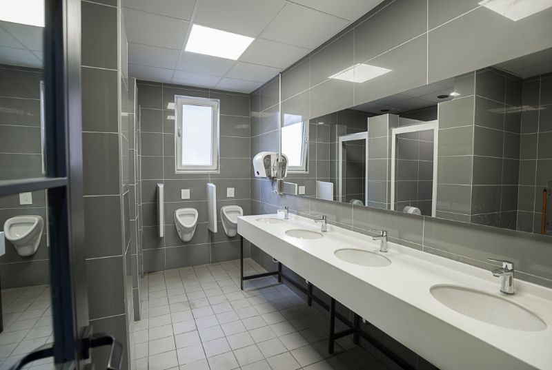Commercial bathroom tiling with light grey floor tiles, dark grey wall tiles, three sinks and three urinals
