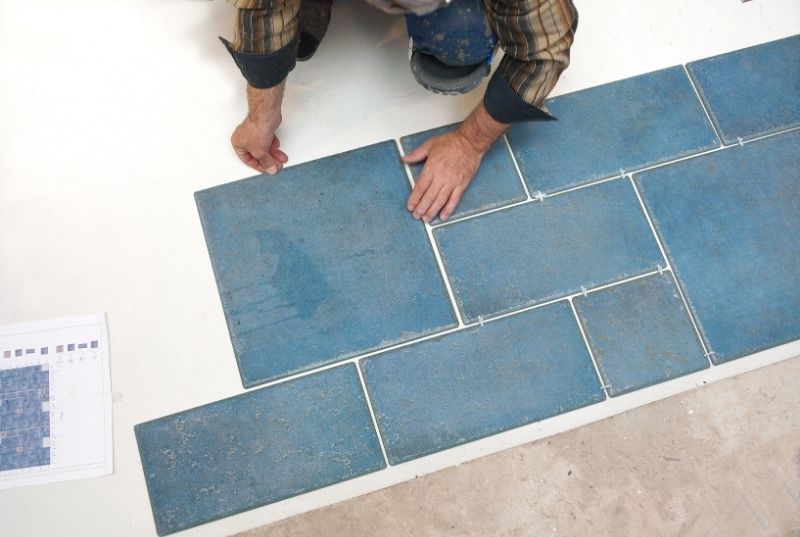 Tiler laying blue and grey floor tiles