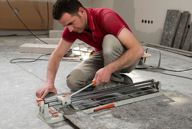Tiler using a cutting tool to cut tiles for a floor installation