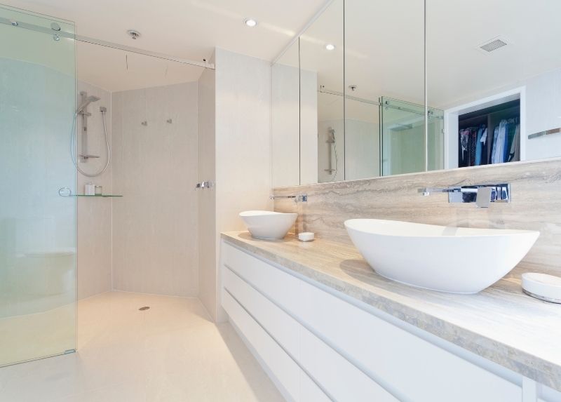 White residential bathroom tiling with a bowl sink over a wooden vanity cabinet