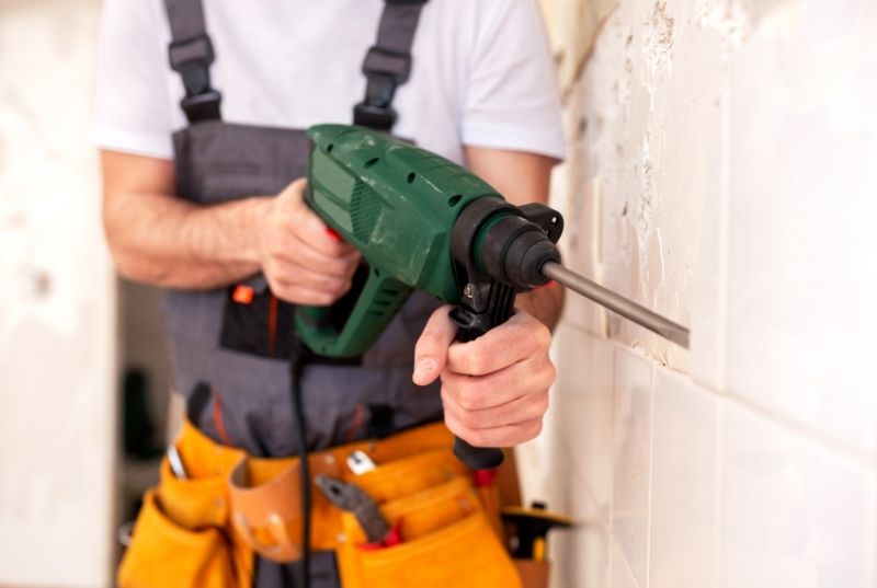 Tiler using a power hack hammer removing a wall tile