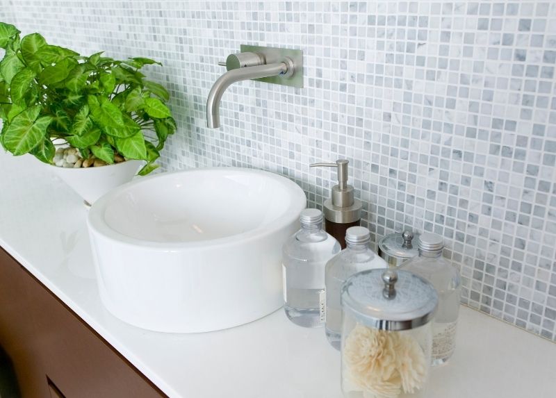 Blue mosaic bathroom tiling with a bowl sink and hand wash products on the vanity