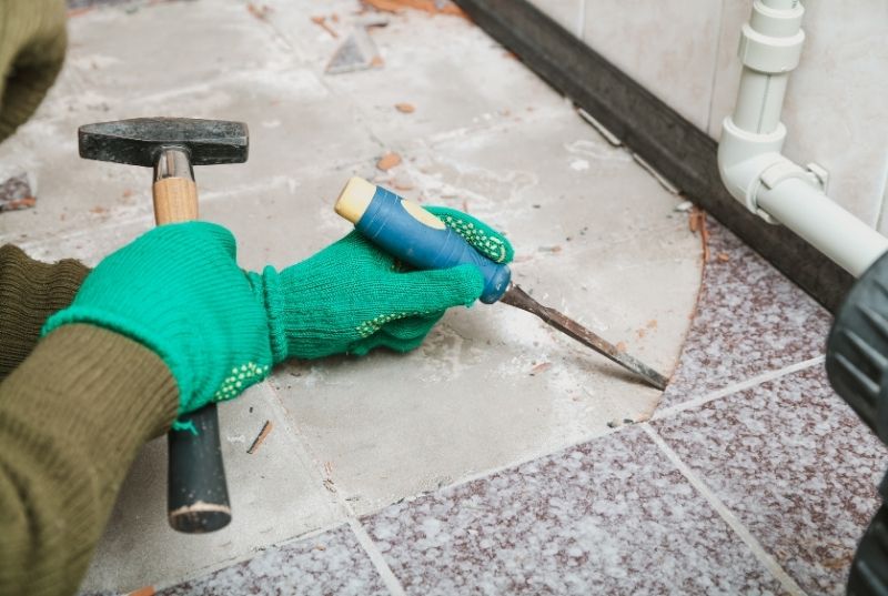 Tiler using chisel and hammer to remove floor tiles