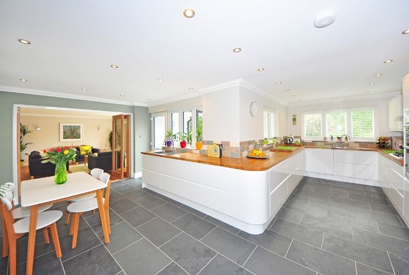 Open-plan residential kitchen with white cabinets and grey ceramic floor tiles