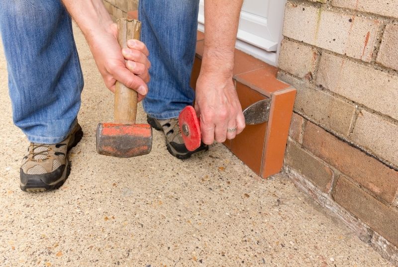 Person removing outdoor tiles using a chisel and a hammer